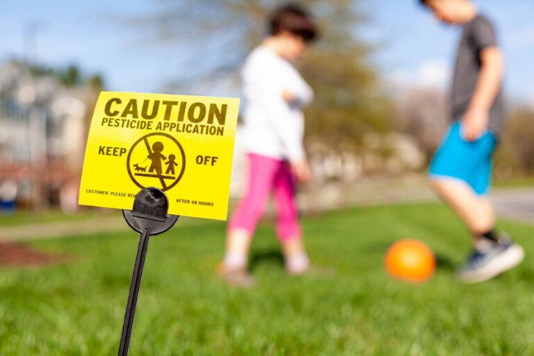 Children Playing Soccer in Front of a Yellow Pesticide Warning Sign